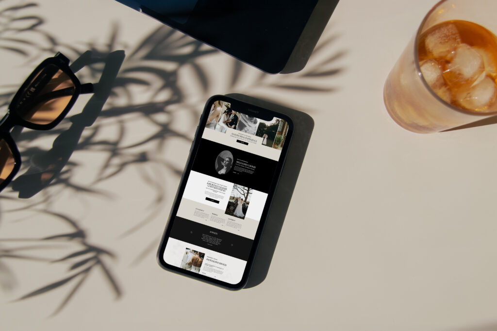 An iphone with a shadow of a plant cast over it with a nice beverage and a pair of sunglasses with orange lenses. The iphone screen shows a mobile website optimized for a wedding photographer in a modern design.